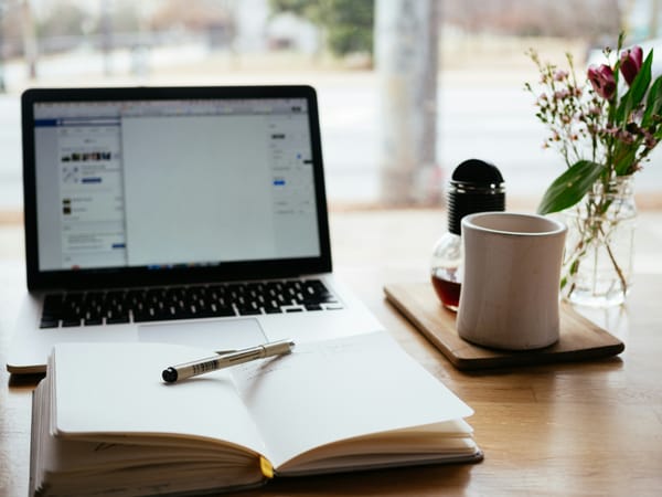 An image of a computer, open book, and coffee mug representing the concept of research.